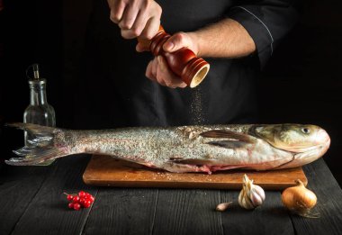 Profesyonel şef mutfakta gümüş sazan balığı balığı hazırlıyor. Aşçı balığın üzerine biber serper. Restoran ya da otel için menü fikri