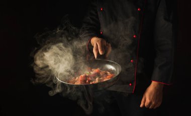 Profesyonel şef sebzeleri kızartma tavasında hazırlar. Sağlıklı vejetaryen yemekleri ve yemekleri karanlık bir arka planda pişirmek. Ücretsiz reklam alanı.