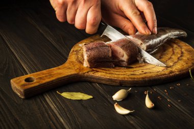 Aşçı, tahta bir kesme tahtasıyla taze Merluccius balığını bıçakla keser. Eski bir tarife göre lezzetli bir balık yemeğinin ev yemeği. Köylü yemekleri.