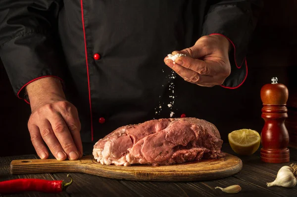 Professional chef sprinkles raw meat with salt. Preparing fresh meat before roasting. Menu concept for restaurant or hotel. European cuisine.