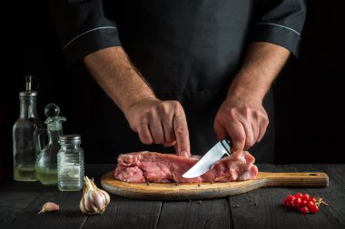 Profesyonel aşçı pişirmeden önce eti bıçakla keser. Lezzetli bir öğle yemeği hazırlamak için mutfak masasındaki baharatlar.