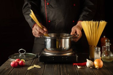 Aşçı, sebzeli bir tencerede İtalyan makarnası hazırlar. Lokanta mutfağında yemek pişirirken aşçı ellerinin yakın çekimi. Avrupa mutfağı.