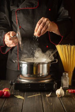 Mutfakta İtalyan spagettisi pişirmek. Şef bir kap kaynar suya tuz ekliyor. Büyük mutfak.