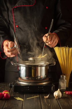 Öğle yemeği için lezzetli çorba pişiriyorum. Mutfakta çalışma ortamı. Şef tencerede spagetti pişiriyor..