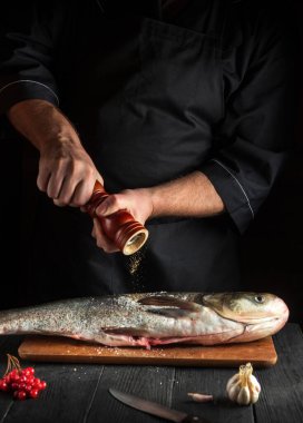 Aşçı mutfakta sazan balığı hazırlıyor. Şef balığın üzerine biber serper. Mutfak masasında çalışma ortamı