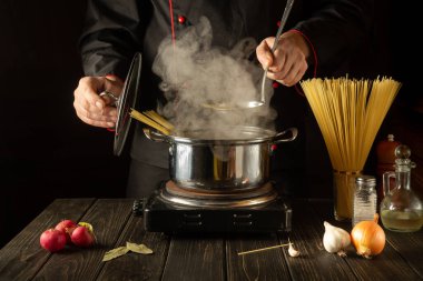 Şef mutfakta bir tencerede spagetti çorbası hazırlıyor. Lezzetli bir öğle yemeği hazırlamak için bir otel fikri. Avrupa mutfağı.