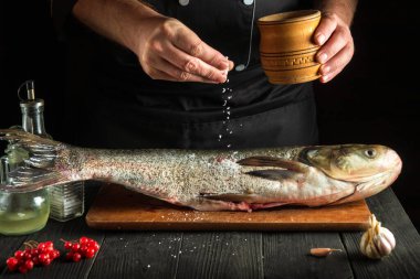 Şef mutfakta gümüş sazan balığı ringası hazırlıyor. Aşçı balığın üzerine tuz serper. Mutfak masasında çalışma ortamı
