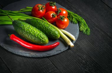 Otel tarifi için bir menü fikri. Taze sebze salatası. Kırmızı domates ve yeşil soğanlı siyah tabakta salatalık..