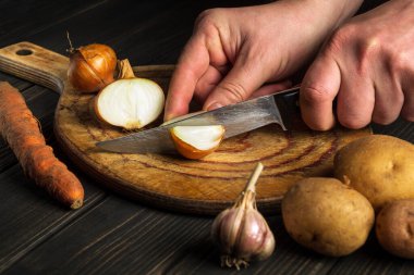Şef öğle yemeği için çorba yapmak için soğanı kesme tahtasının üzerinde bıçakla keser. Sebze diyeti fikri. Mutfak masasında çalışma ortamı