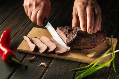 Şefin elleriyle akşam yemeği hazırlamadan önce fırında et dilimliyorum. Üst görüş aşçılık süreci konsepti. Köylü yemekleri..