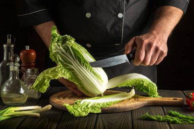 Şef mutfak masasında taze sebzelerle birlikte salata için taze Napa lahanasını bıçakla keser. Lezzetli yemekler pişirme kavramı