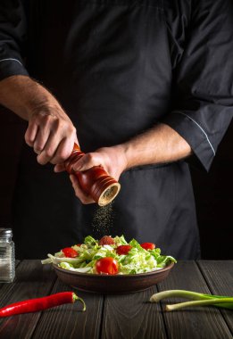 Profesyonel şef mutfaktaki taze sebze salatasına biber ekler. Bir değirmeni tutan aşçı ellerinin yakın çekimi. Lezzetli yemekler pişirme kavramı