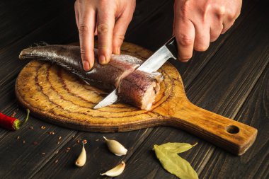 Bıçaklı şef tahta kesme tahtasına taze Merluccius balığı kesti. Eşsiz bir tarifle ulusal bir balık yemeğinin ev yemeği..