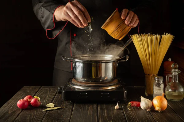 Mutfakta İtalyan spagettisi pişirmek. Şef bir kap kaynar suya tuz ekliyor. Büyük mutfak.