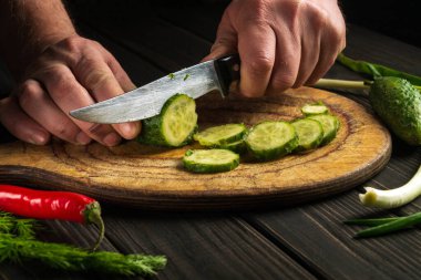 Bir ahçının elleri bıçakla kesme tahtasındaki salatalığı keserken. Taze sebzeli lezzetli kahvaltı salatası.