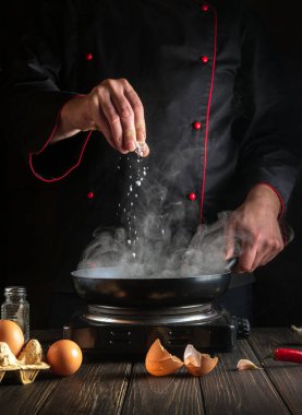 Aşçı tavada yumurta pişirirken tuz ekler. Mutfak masasında çalışma ortamı. Restoran ya da otel için menü fikri