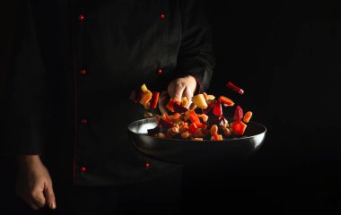 Profesyonel şef taze sebzeleri kızartma tavasında hazırlar. Sağlıklı vejetaryen yemekleri ve karanlık arka planda yemekler için tarif. Ücretsiz reklam alanı
