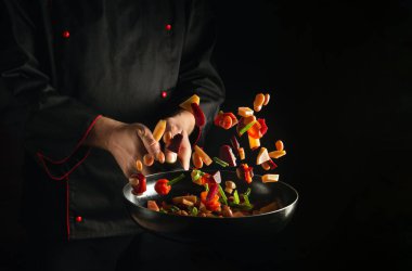Professional chef prepares fresh vegetables in a frying pan. Recipe for healthy vegetarian food and meals on a dark background. Free advertising space.