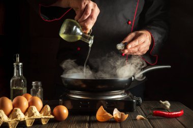 Aşçı tavada yumurta pişirirken sebze yağı ekler. Mutfak masasında çalışma ortamı. Restoran ya da otel için menü fikri