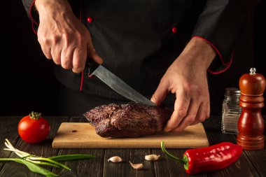 Aşçı elleri bifteği tahta kesme tahtasında bıçakla dilimliyor. Yemek hazırlama süreci konsepti. Çabuk yemek..