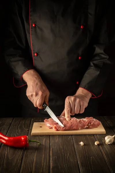 The chef cuts raw beef meat on a cutting board before baking. Asian cuisine. Hotel menu recipe idea.