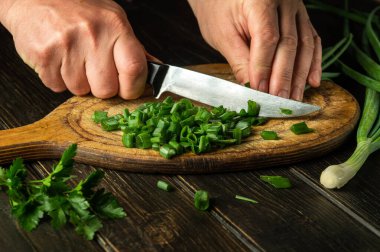 Slicing green onions on a cutting board with a knife for cooking vegetarian food. Peasant dish.