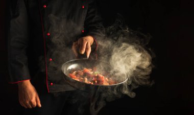 Şef kızartma tavasında sebze hazırlar. Siyah arka planda sağlıklı vejetaryen yemeği ve yemek pişirmek. Ücretsiz reklam alanı