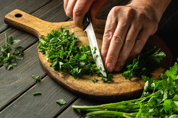 Vejetaryen yemeği pişirmek için kesme tahtasındaki yeşil maydanozu bıçakla kesmek. Köylü yemeği..
