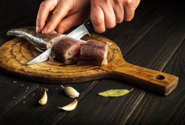 Şef taze Merluccius balığını tahta bir kesme tahtasıyla bıçakla keser. Eski bir tarife göre lezzetli bir balık yemeğinin ev yemeği.