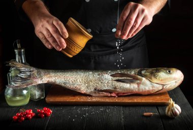 Şef mutfakta gümüş sazan balığı balığı hazırlıyor. Aşçı balığın üzerine tuz serper. Mutfak masasında çalışma ortamı