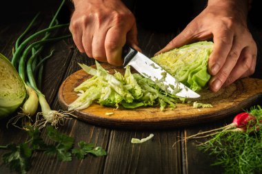 Kesme tahtasında lahana dilimlemek. Akşam yemeği için taze sebzeli lezzetli salata. Mutfakta yemek pişirirken bıçaklı bir şefin elleri.