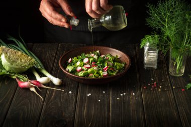 Şef lezzetli bir salatayla birlikte bir tabağa sebze yağı ekler. Taze sebzelerle diyet kahvaltısı.