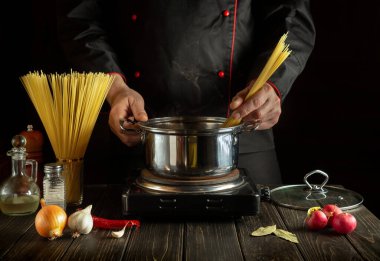 Şef sebzeli bir tencerede İtalyan makarnası hazırlıyor. Mutfakta yemek pişirirken ellerin yakın plan çekimi.