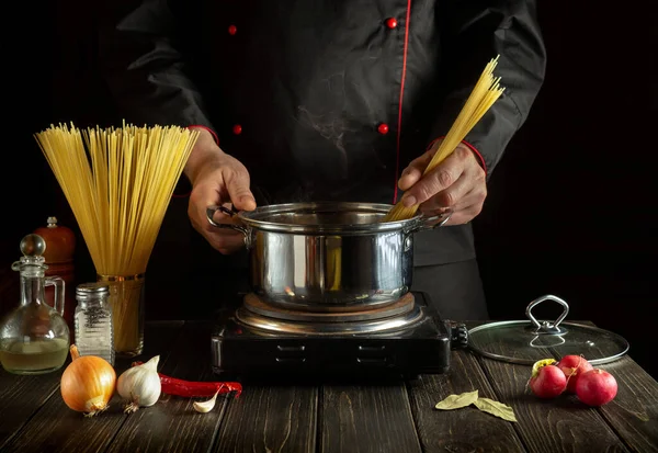 Şef sebzeli bir tencerede İtalyan makarnası hazırlıyor. Mutfakta yemek pişirirken ellerin yakın plan çekimi.