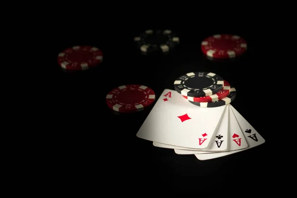 Playing cards on a black table with a winning combination four of a kind or quads in game poker and chips in the background.
