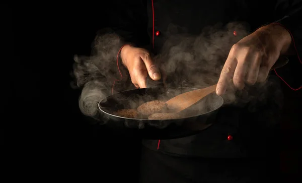 The chef is frying burger cutlets in a frying pan. Close-up of a cook\'s hands with a hot pan in the kitchen. Free space for advertising
