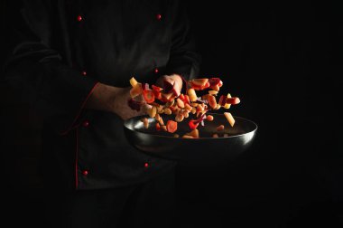 Profesyonel şef taze sebzeleri kızartma tavasında hazırlar. Büyük mutfak ve yemek tarifi koyu arka planda. Ücretsiz reklam alanı