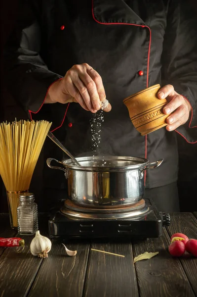 Profesyonel aşçı saksıya tuz ekliyor. Öğle yemeği için lezzetli çorba pişiriyorum. Mutfakta çalışma ortamı