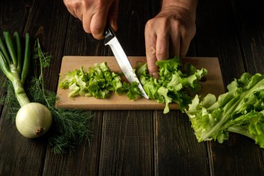 Şef ellerinin yakın plan çekimi. Vejetaryen yemeği hazırlamak için kesme tahtasına yeşil yaprak serpiştirmek..