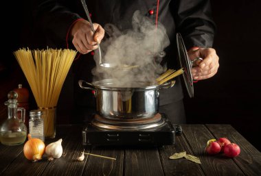 Profesyonel şef mutfakta bir tencerede spagetti çorbası hazırlar. Lezzetli bir yemek hazırlamak için bir otel fikri