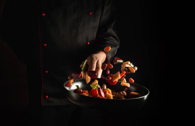 Şef kızartma tavasında taze sebzeler hazırlar. Büyük mutfak ve yemek tarifi koyu arka planda. Ücretsiz reklam alanı