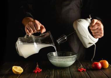 Profesyonel şef, elektrikli el mikseri kullanarak mutfakta meyveli milkshake hazırlıyor. Aşçı derin bir tabağa süt döker. Otel için lezzetli tarif menüsü
