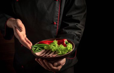 Şef bir tabak doğranmış et ve sebze getirdi. Karanlık arka planda yemek pişirme kavramı.