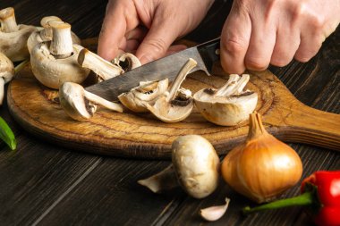 Şef ahşap bir kesme tahtasıyla Agaricus mantarı keser. Aşçı ellerinin yakın çekimi. Köylü yemekleri.
