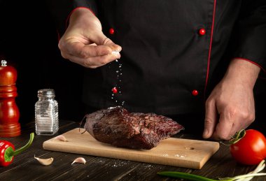 Şef pişmiş sığır etine tuz serpiyor. Otel için lezzetli yemekler pişirme konsepti