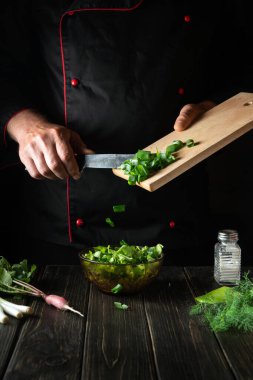 Taze sebze salatasına doğranmış yeşil soğan ekliyorum. Aşçı mutfakta lezzetli yemekler pişirirken.