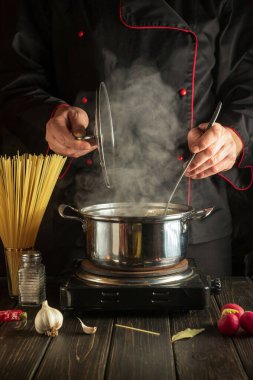 Profesyonel şef mutfakta bir tencerede spagetti çorbası hazırlar. Lezzetli bir yemek hazırlamak için bir otel fikri