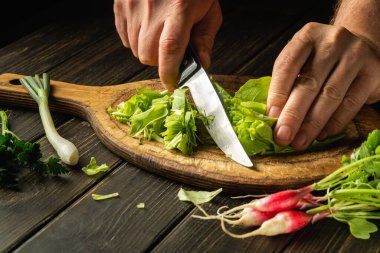 Bir aşçının eli, vejetaryen yemeği hazırlamak için bir bıçakla kesme tahtasının üzerinde yeşil yapraklar keser..