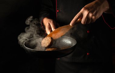 Şef kızartma tavasında hamburger pirzolası pişiriyor. Mutfakta sıcak bir tavayla bir aşçının ellerine yakın çekim. Reklam için boş alan.