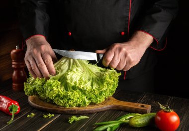 Şef kesme tahtasının üzerinde bir bıçakla marul keser. Vejetaryen yemeği.